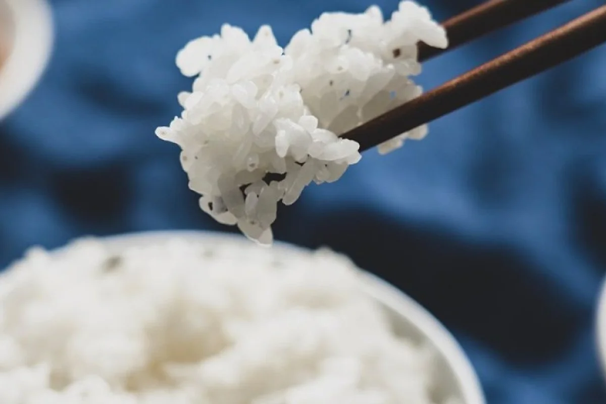close up of cooked fluffy rice grains with chopsticks and rice vinegar bottle