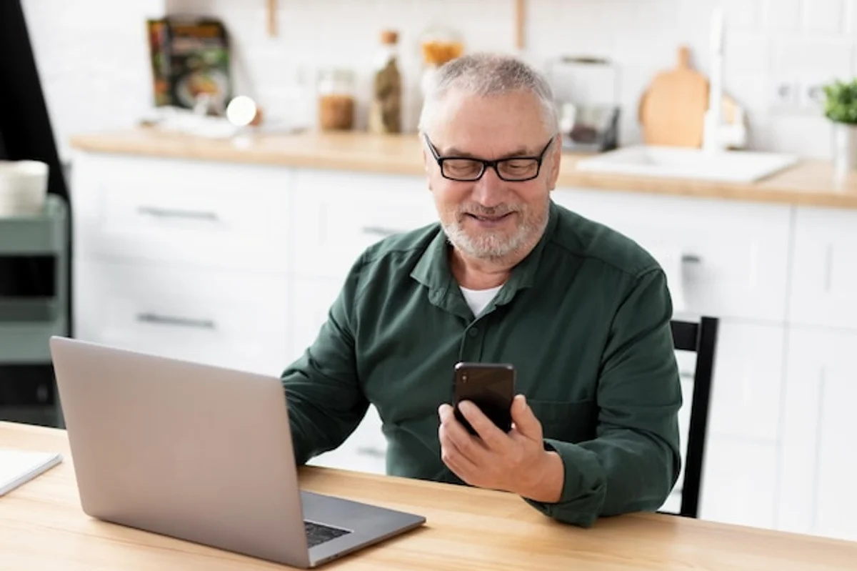 senior using smartphone budget app at kitchen table