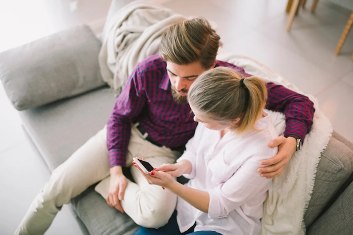 two people sitting together on sofa, both using smartphones, feeling distant